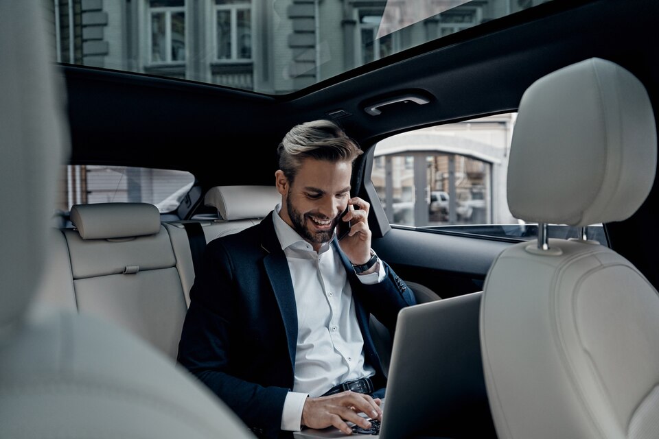 Discussing business details. Young man in full suit talking on smart phone and smiling while sitting in the car